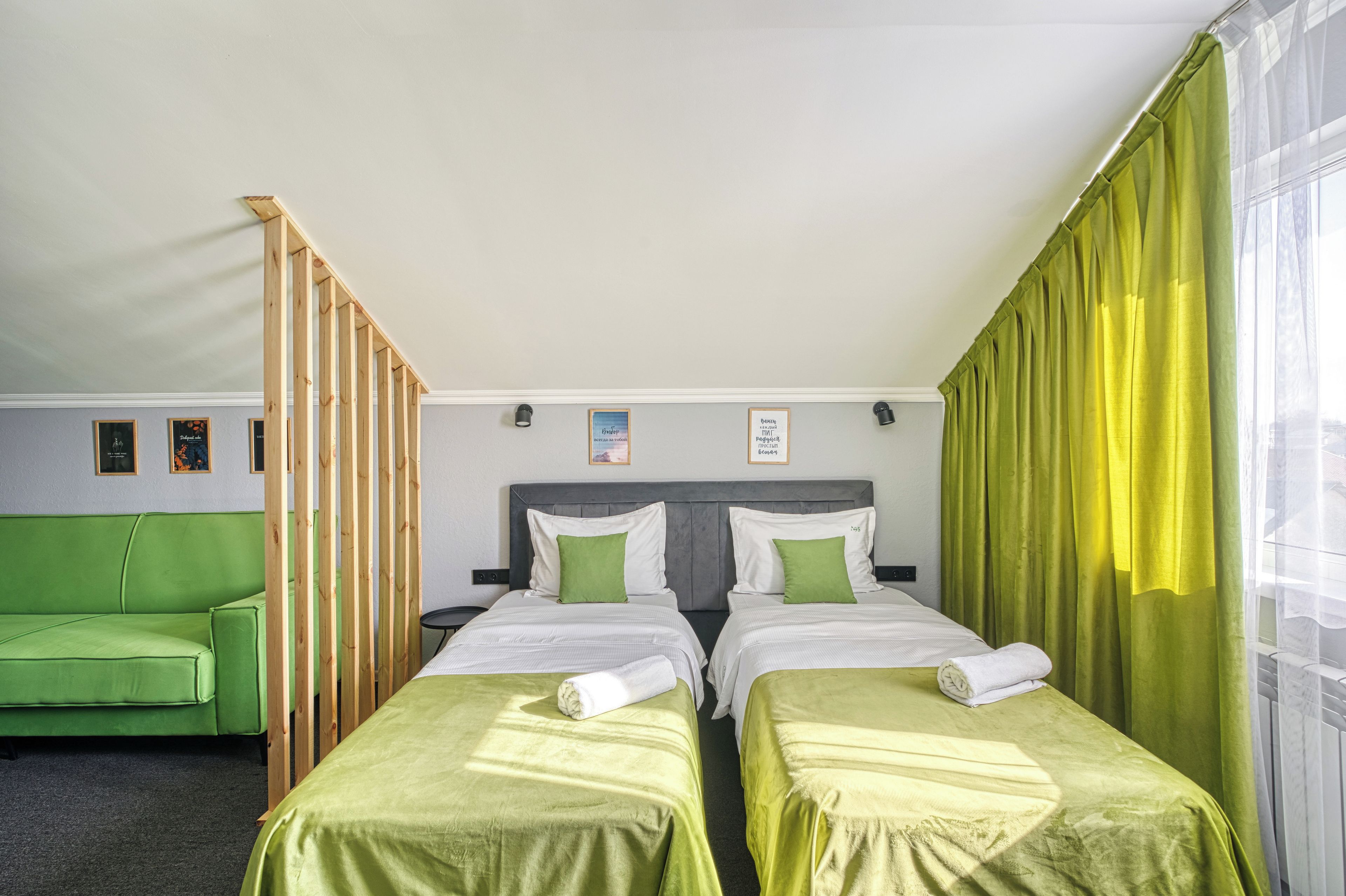 A hotel room with two single beds, a green sofa, and a window with yellow curtains.