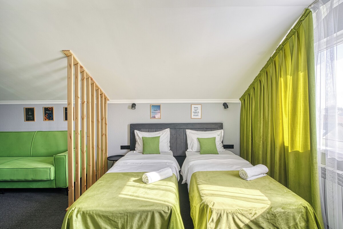 A hotel room with two single beds, a green sofa, and a window with yellow curtains.
