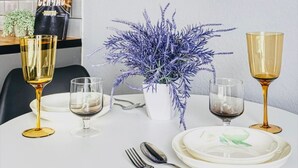 A dining table set with plates, cutlery, and glasses, a potted plant, and a flat-screen TV mounted on the wall. - The Apartamens 95 (Almaty)