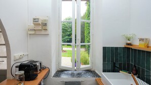 Un baño con una puerta blanca que da a un jardín, un lavamanos con espejo y un estante con artículos de aseo.