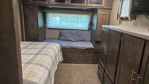 Interno di un camper compatto con un letto, un piccolo oblò e armadietti integrati.