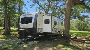 Ein Rockwood ULTRA LITE Wohnmobil steht in einer bewaldeten Gegend, im Hintergrund sind Bäume und ein Picknicktisch zu sehen.