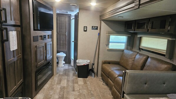 A narrow hallway with a toilet, a trash can, and a brown leather couch.