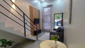 A modern living room with a staircase, a round wooden table with a vase, a sofa, and a TV mounted on the wall. - Romantic 1-bedroom apartment with AC in fantastic El Castillo (El Castillo)