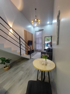 Ein modernes Wohnzimmer mit Treppe, einem runden Holztisch mit Vase, einer Couch und einem an der Wand montierten Fernseher.