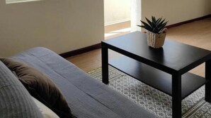 Ein Zimmer mit einem Bett, einem kleinen Tisch mit Pflanze und zwei Fenstern mit Blick auf eine Hügelkuppe.