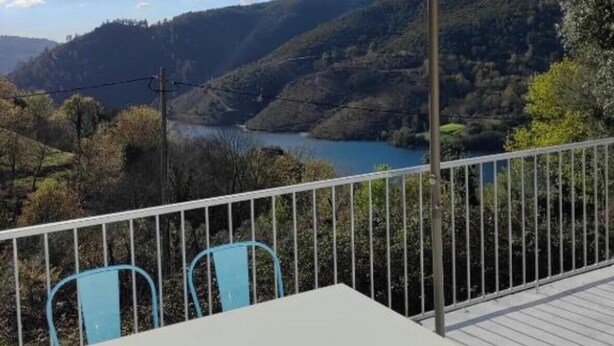 Eine Terrasse mit Tisch und Stühlen mit Blick auf ein Tal und einen See.