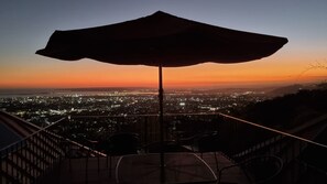 Terraza con sombrilla, sillas y vista a la ciudad al atardecer.