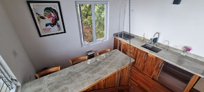 A kitchen with a marble countertop, wooden cabinets, a built-in dishwasher, and a window with a view of greenery.