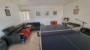 Una habitación con un sofá de cuero negro, una mesa de ping pong, un tambor rojo y un teclado.