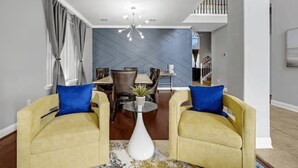 Ein Wohnzimmer mit zwei gelben Sesseln, einem Couchtisch, einem Essbereich mit Tisch und Stühlen sowie einer Treppe, die in eine obere Ebene führt.