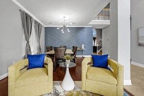 Ein Wohnzimmer mit zwei gelben Sesseln, einem Couchtisch, einem Essbereich mit Tisch und Stühlen sowie einer Treppe, die in eine obere Ebene führt.