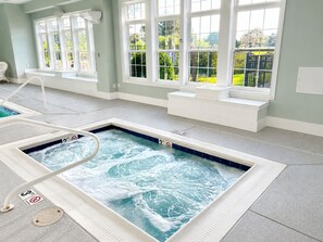 Ein Wellnesspool mit Whirlfunktion, einer Sitzgelegenheit am Fenster und Blick auf einen Garten.