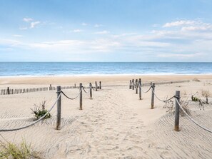 Ein sandiger Strand mit einem Holzzaun und einer Seilsperre, die zum Meer führt.