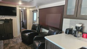 A kitchenette with a coffee maker, toaster, and jar. There are two black leather chairs and a table. A TV is mounted on the wall. - Wildwood camper #5  at Heaven's Ridge Campground (Fair Play)
