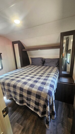 Une chambre à coucher avec une couvre-lit à carreaux, une tête de lit sombre, un miroir et un plancher en bois.