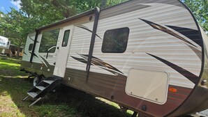 A recreational vehicle with a sliding door, a small window, and a step leading to the entrance. - Wildwood camper #5  at Heaven's Ridge Campground (Fair Play)