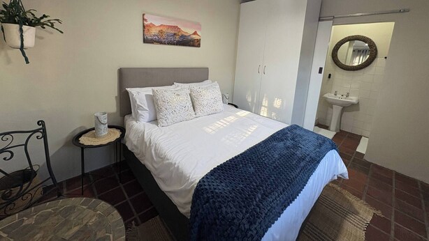 Camera da letto con un letto, un comodino, una pianta pensile, un quadro, un armadio e uno specchio, oltre a un bagno con un lavandino.