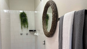 Un bagno con piastrelle bianche, uno specchio, un porta asciugamani e una zona doccia.