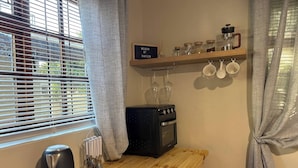Una cucina con fornello, bollitore e un ripiano in legno con tazze e barattoli.