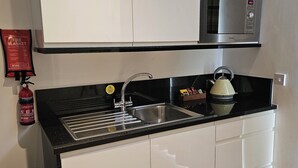 Una cocina moderna con armarios blancos, un lavamanos de acero inoxidable, un microondas y un extintor.