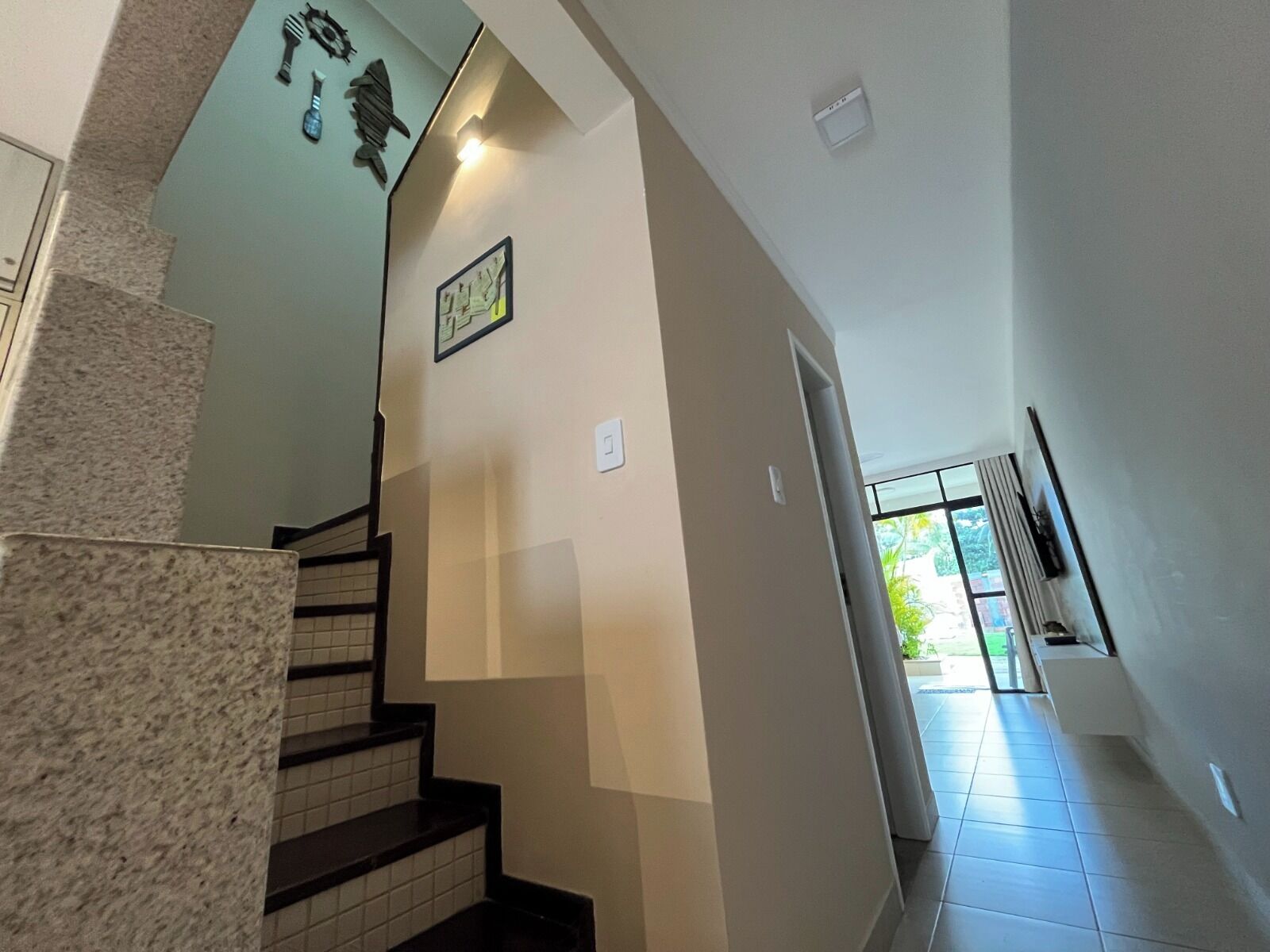 Un escalier avec une rampe, un luminaire fixé au mur et une porte donnant sur un espace extérieur.