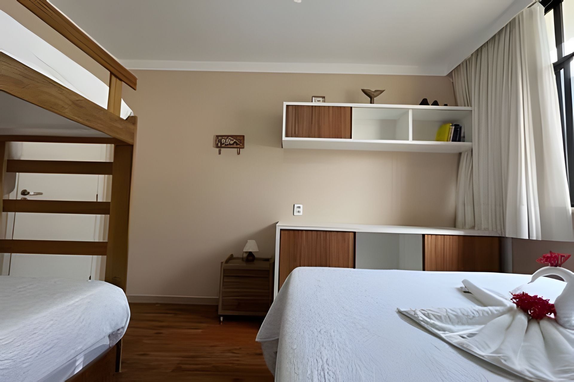 Et hotelværelse med køjeseng, et sengebord, en lampe, et klædeskab og et vindue med gardiner.