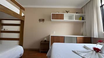 Een hotelkamer met een stapelbed, nachtkastje, lamp, kledingkast en raam met gordijnen.