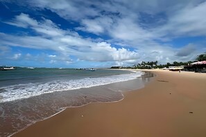 A beach with a sandy shore, calm sea, and a clear sky with clouds. - Guarajuba, beachfront two-bedroom duplex (Camaçari)