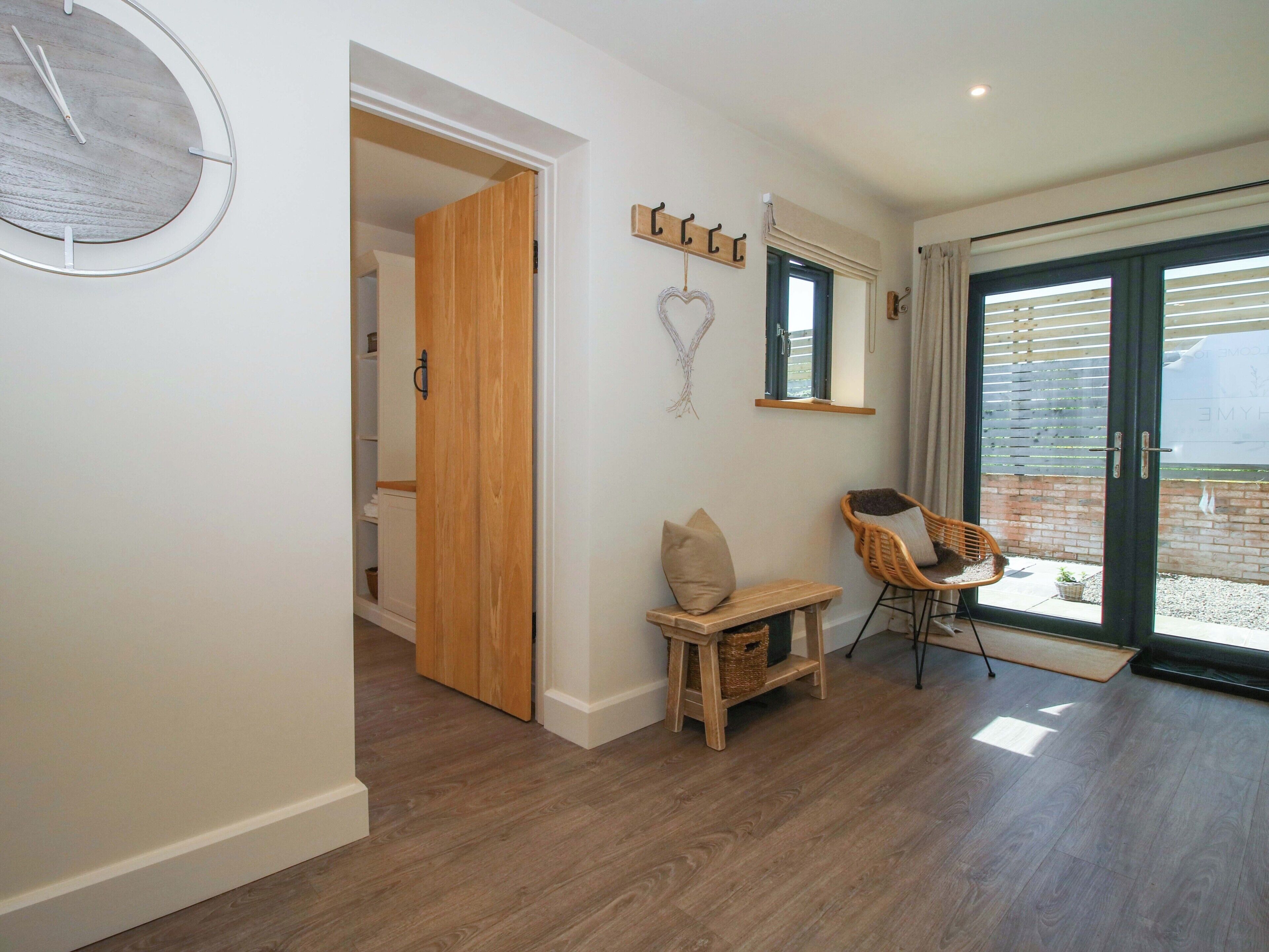 A room with a wooden floor, a bench, a chair, a wall clock, and a sliding glass door leading to an outdoor area.