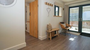 Ein Zimmer mit Holzboden, einer Bank, einem Stuhl, einer Wanduhr und einer Glastür zum Außenbereich.