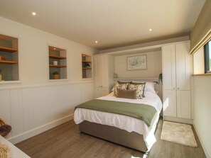 A bedroom with a bed, built-in shelving, a window, and a door. - Thyme Away (Bucknell)