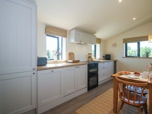 A modern kitchen with white cabinets, a built-in oven, and a dining area with a wooden table and chairs. - Thyme Away (Bucknell)