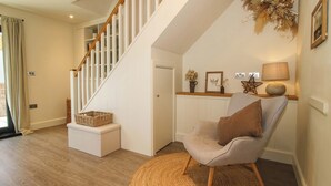 Eine Treppe mit weißen Geländern, einem gewebten Teppich, einem gepolsterten Stuhl und einer Wandlampe.