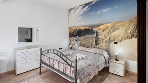 Un dormitorio con cama, mesita de noche, cómoda, espejo y un gran mural en la pared.