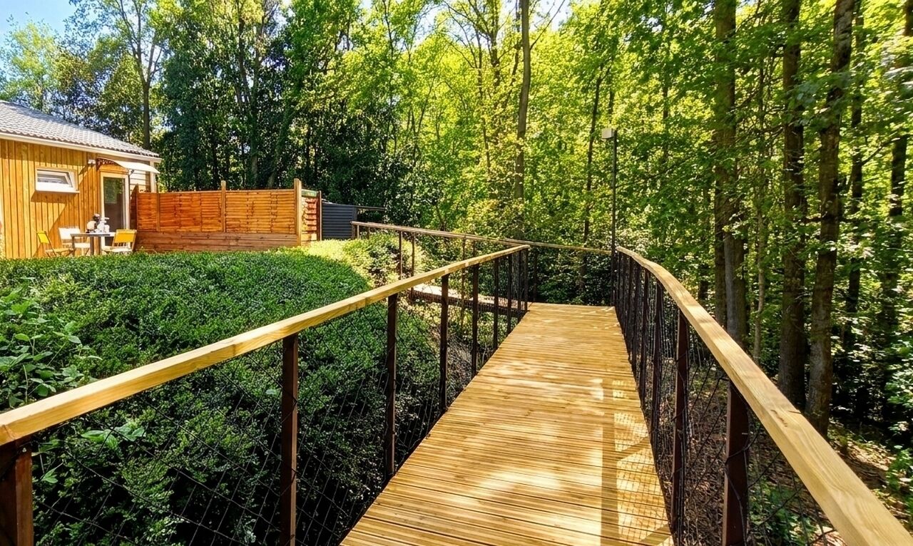 Une terrasse en bois qui mène à un bâtiment entouré d’une végétation luxuriante.