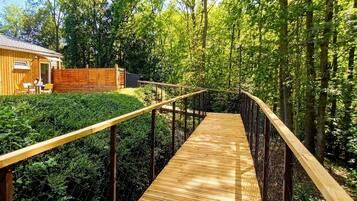 Une terrasse en bois qui mène à un bâtiment entouré d’une végétation luxuriante.