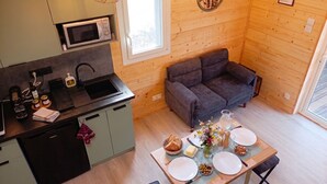 A compact kitchen with a microwave, sink, and modern appliances. A cozy seating area with a sofa and a dining table set for two, featuring a pitcher, flowers, and a bowl of olives. - Gîte Hydra Nature (Conteville)