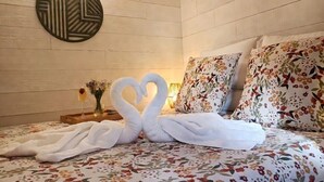 A hotel room with a bed, floral bedding, a wall-mounted decorative piece, and a vase with flowers. - Gîte Hydra Nature (Conteville)