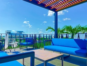 Eine Dachterrasse mit blauen Sitzgelegenheiten, einer Pergola und Blick auf die Stadtlandschaft.