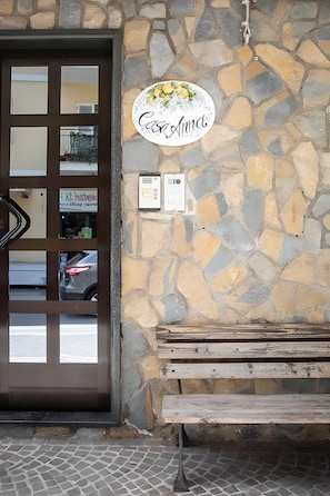 A stone wall with a sign reading 'Casa Anna,' a wooden bench, and a door with a reflection of a car and a building. - Casa Anna Standard Faito View in Pimonte – Comfort e Vista Montagna (Pimonte)