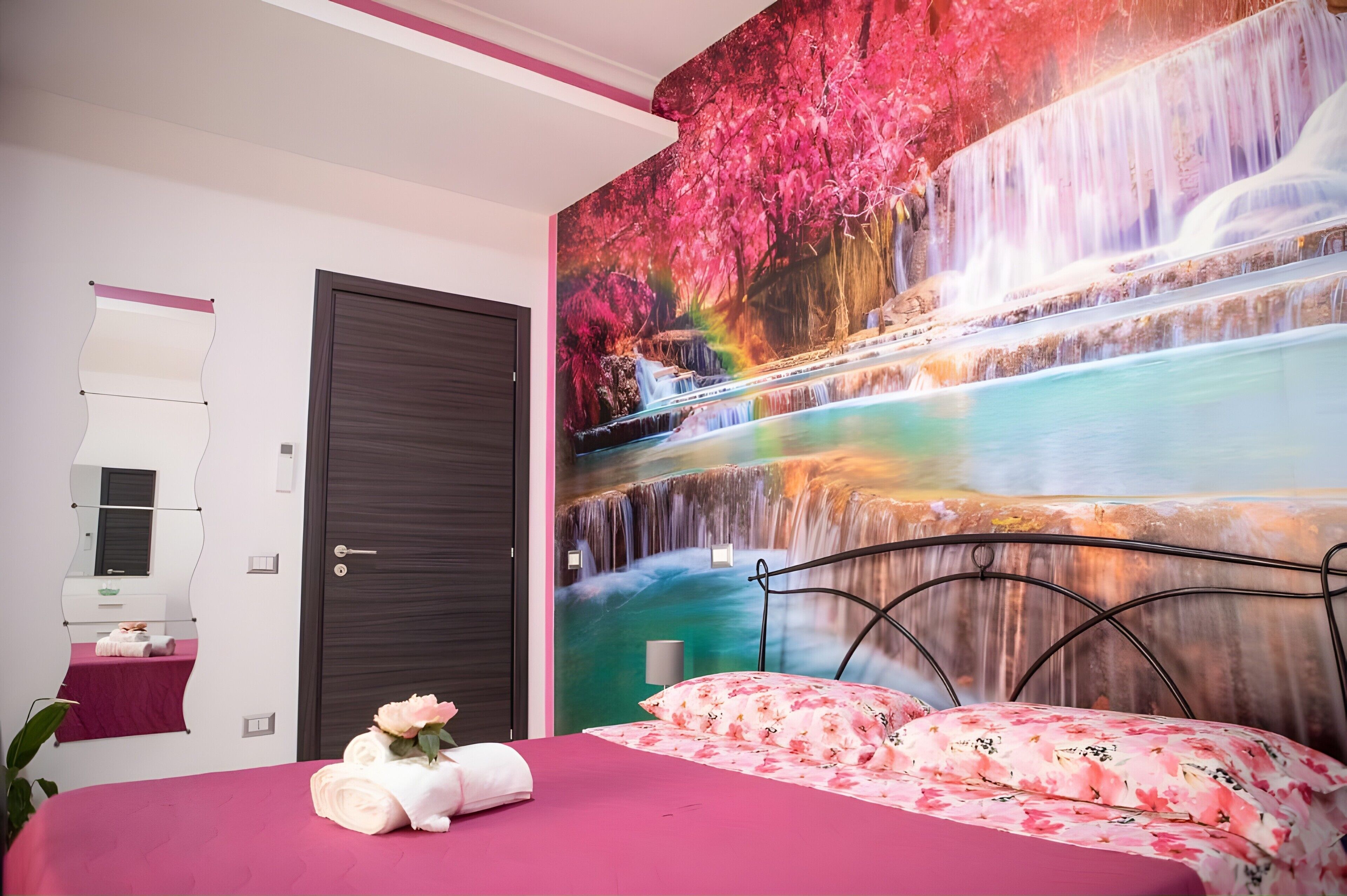 Un dormitorio con cama, espejo en la pared, puerta y un mural grande de una cascada.