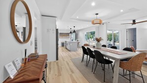 A modern kitchen with white cabinets, a central island, and a dining area with a wooden table and black chairs. - Coastal Largo Retreat, Pool, Minutes to Indian Rocks Beach, Dog Friendly (Largo)