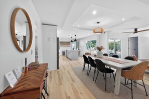 Eine moderne Küche mit weißen Schränken, einer zentralen Kochinsel und einem Essbereich mit Holztisch und schwarzen Stühlen.