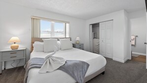 A hotel room with a bed, two bedside tables, a lamp, a window, a closet, and a door. - Coastal Largo Retreat, Pool, Minutes to Indian Rocks Beach, Dog Friendly (Largo)