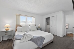 Ein Hotelzimmer mit Bett, zwei Nachttischen, einer Lampe, einem Fenster, einem Schrank und einer Tür.