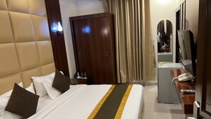 A hotel room with a large bed, a desk with a telephone, a mirror, and a door. - ROYALTY GROUP (Riyadh)