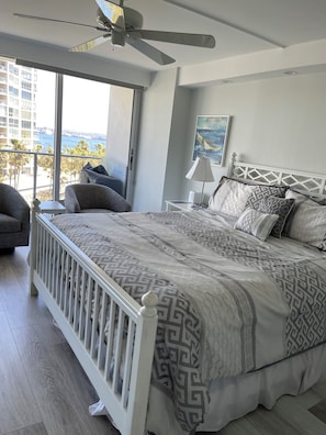 Ein Schlafzimmer mit einem großen Bett, einem Deckenventilator, Blick auf den Ozean und eine Stadtsicht.