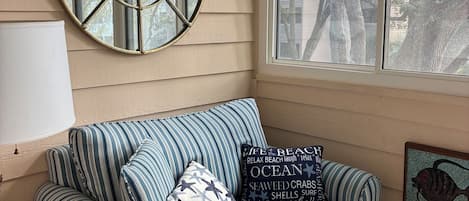 A striped sofa with decorative pillows, a round mirror, and a framed artwork on a wall.