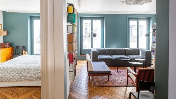 Una habitación con una cama, un sofá gris, una mesita y una estantería.